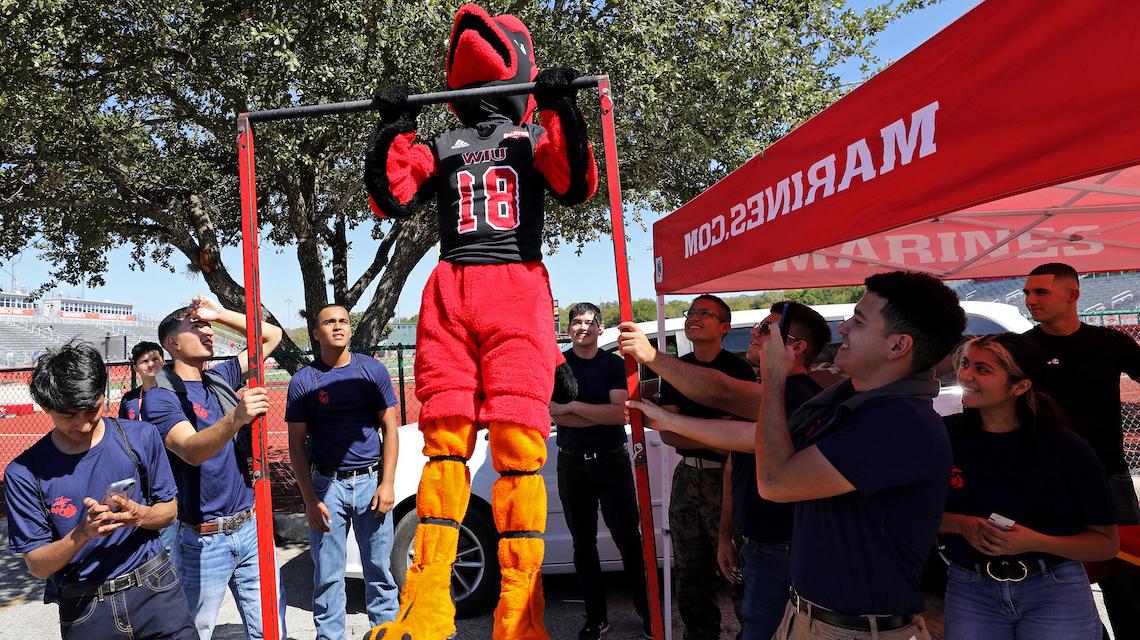 Red The Cardinal doing pull-ups at the Marine Corps tailgate booth 