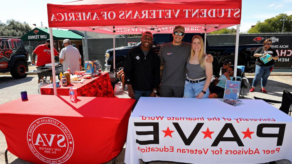 Three student veterans standing at a Peer Advisors for Veteran Education and Student Veterans of America tailgate table